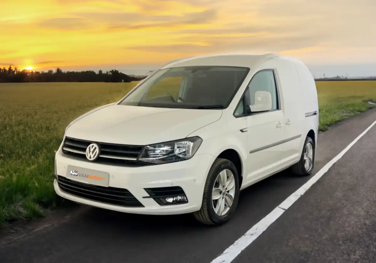a white volkswagen caddy is driving down a country road at sunset.