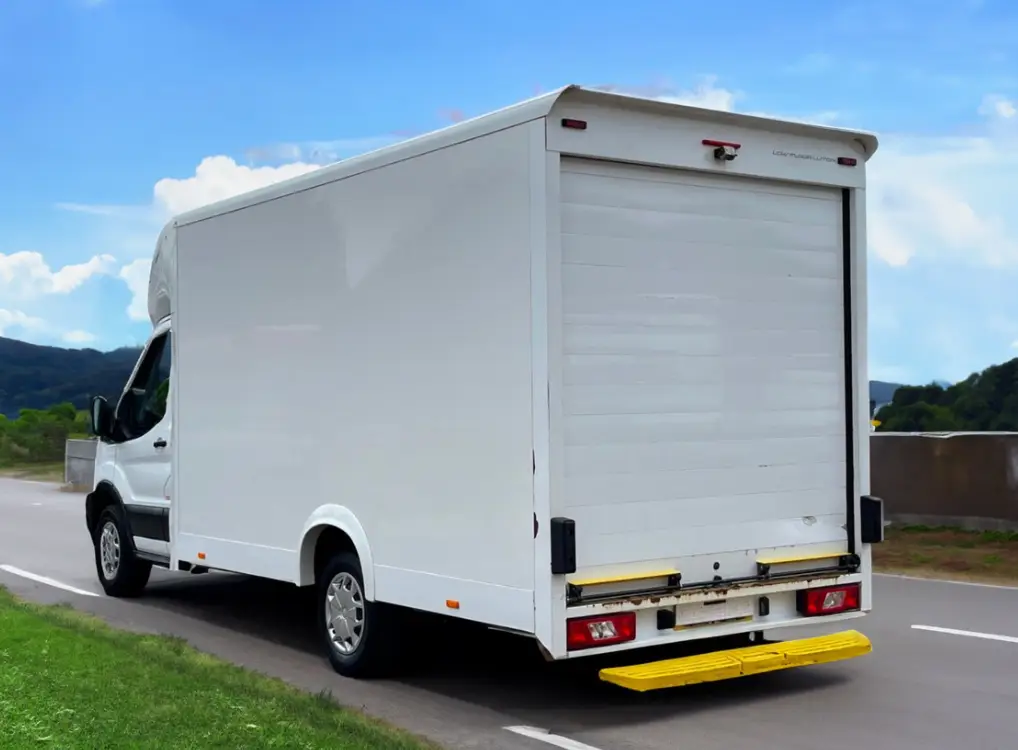 a white Ford Transit Low Loader is driving down the road.