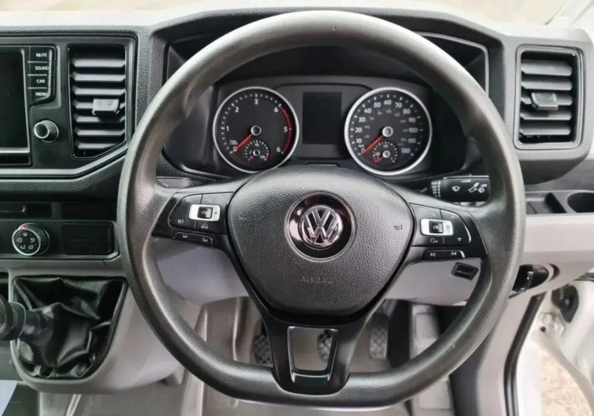 The inside cab of a volkswagen crafter. A black steering wheel with the VW logo in the middle. There is milage clock on the dash.